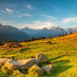 Breathtaking view of Tatra Mountains at sunset with vibrant green fields and rocky foreground.